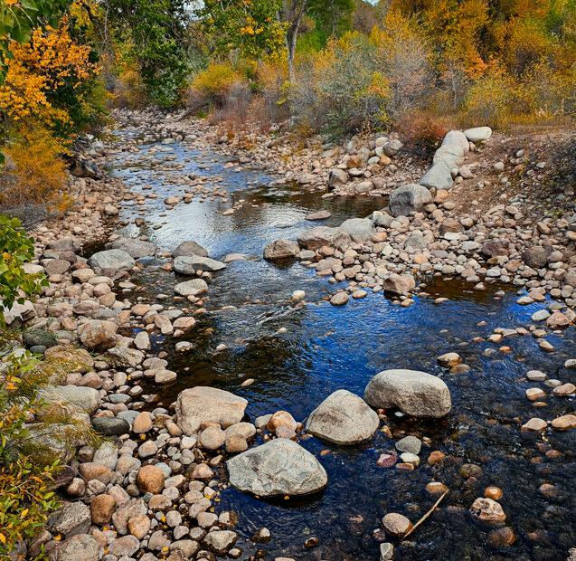 Rocks lining the banks of a stream with fall foliage around.